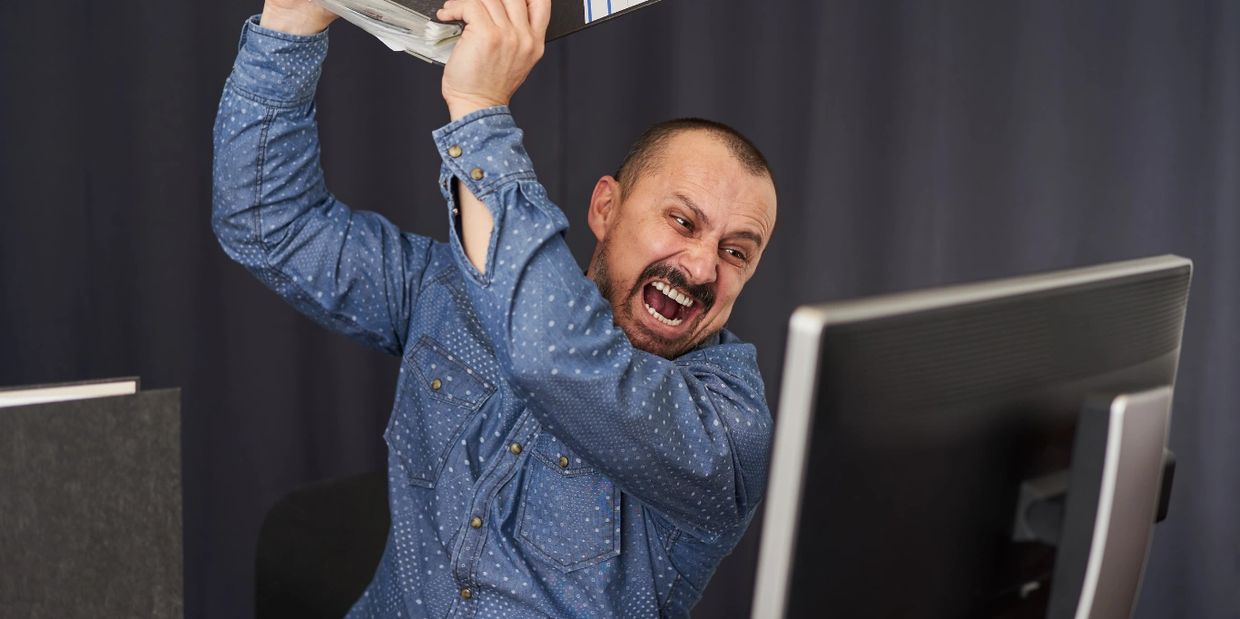 Angry man about to hit computer with a keyboard.