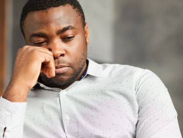 Man looking thoughtful and concerned while resting his face on his hand.