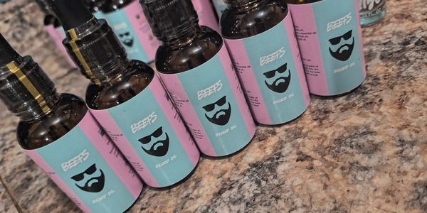 Rows of beard oil bottles with blue and pink labels on a granite countertop.