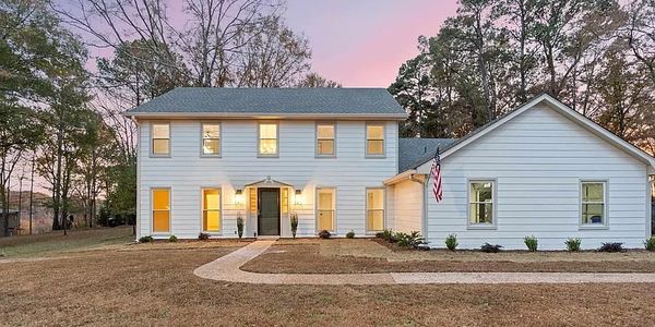 Two-story white house with warm interior lights at dusk and a large front yard.