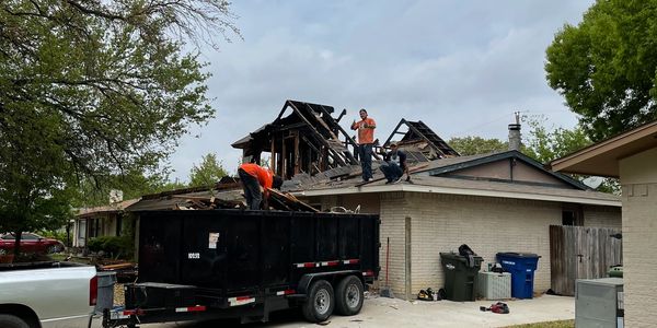 Workers dismantling a damaged roof, loading debris into a trailer.