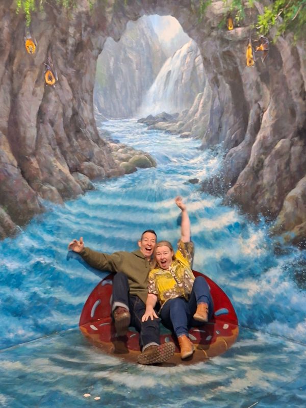 Two people joyfully posing on a 3D water ride mural.