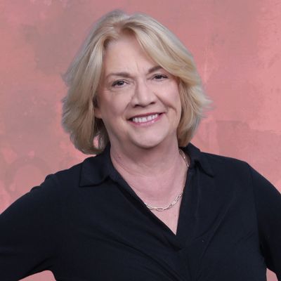 Smiling middle-aged woman with blonde hair in a black top against a pink background.