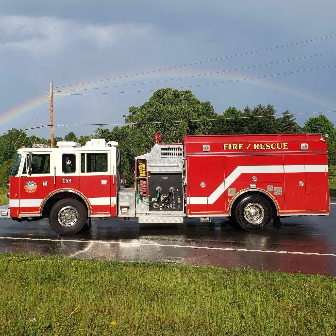Red and white fire rescue truck parked on wet road with a rainbow in the sky.