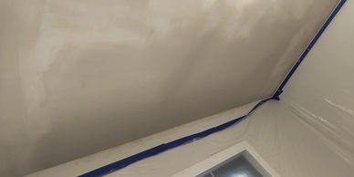 Ceiling with partial paint job and taped plastic sheet covering walls.