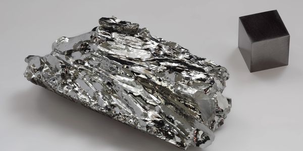 A shiny metallic crystal and a dark metallic cube on a white surface.
