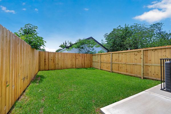 Small fenced grassy backyard with blue sky.