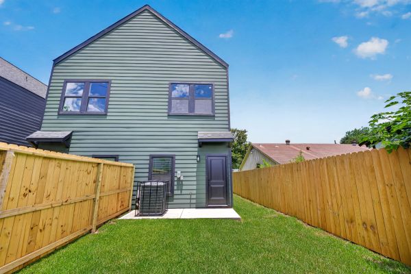 Backyard of a modern house with green siding and wooden fences.