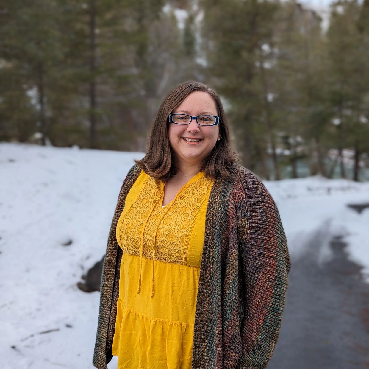 Picture of Judy Jagiello, PsyD wearing yellow top in forested area with snow on the ground
