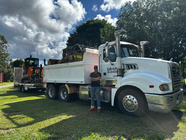 Man standing beside a large white truck with construction equipment on trailer.