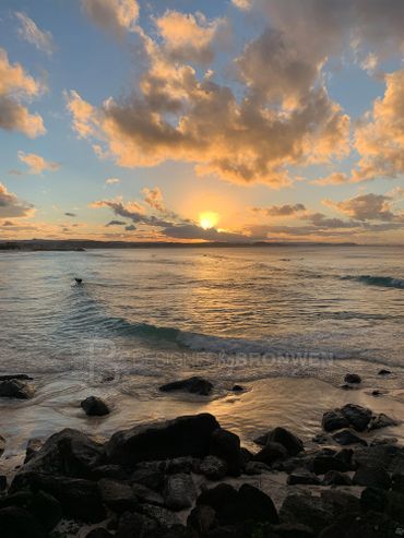 Sunset over a rocky shoreline with scattered clouds in the sky.
