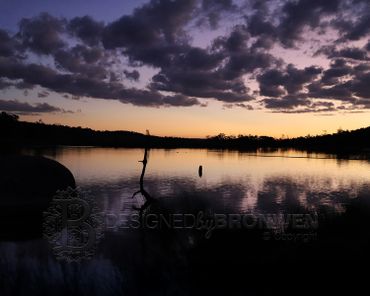 Serene lake at sunset with silhouetted trees and dramatic clouds.