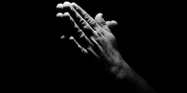 A pair of hands pressed together in prayer with dramatic lighting.