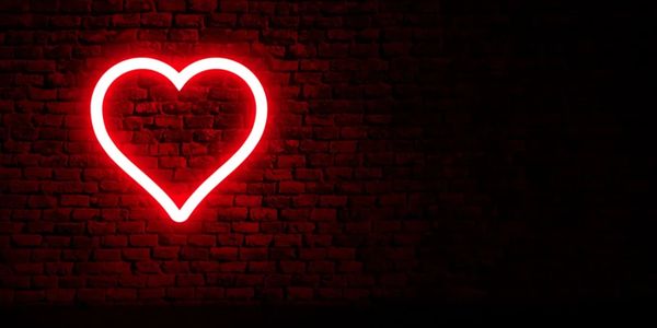 Red neon heart glowing on a dark brick wall.