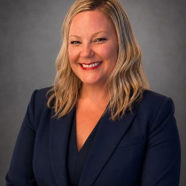 Smiling woman in a navy blazer against a gray background.
