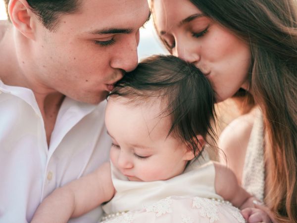Parents lovingly kiss their baby on the head in a tender moment.