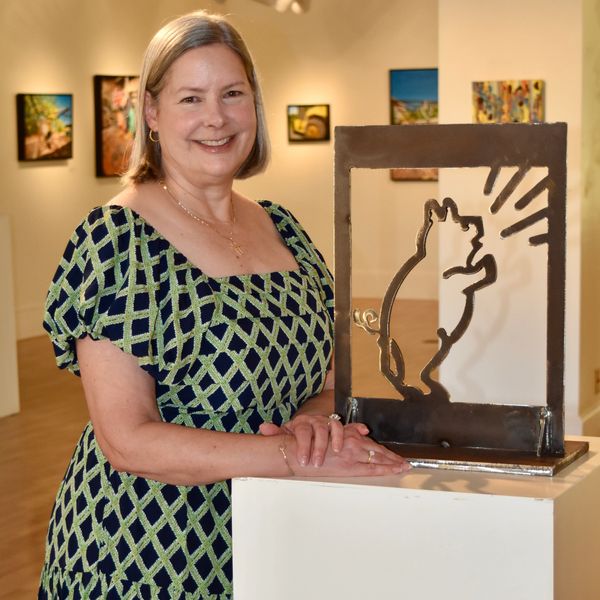 Woman stands next to a metal cat sculpture in an art gallery.