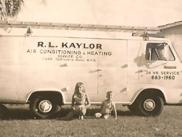 Two children sit on the grass beside an old service van