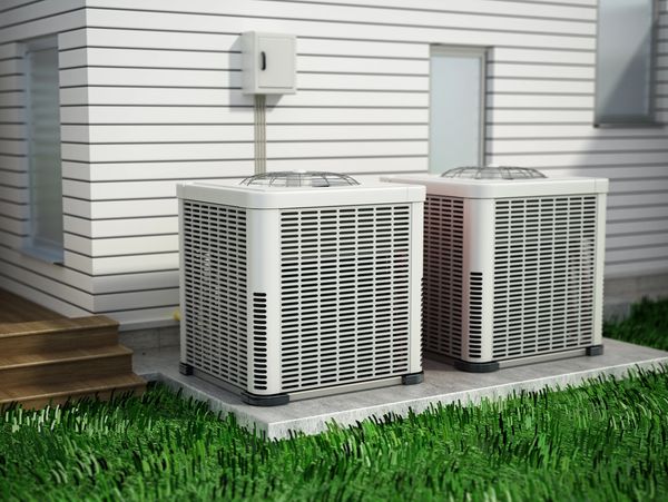 Two white air conditioning units sit on a concrete pad beside a house