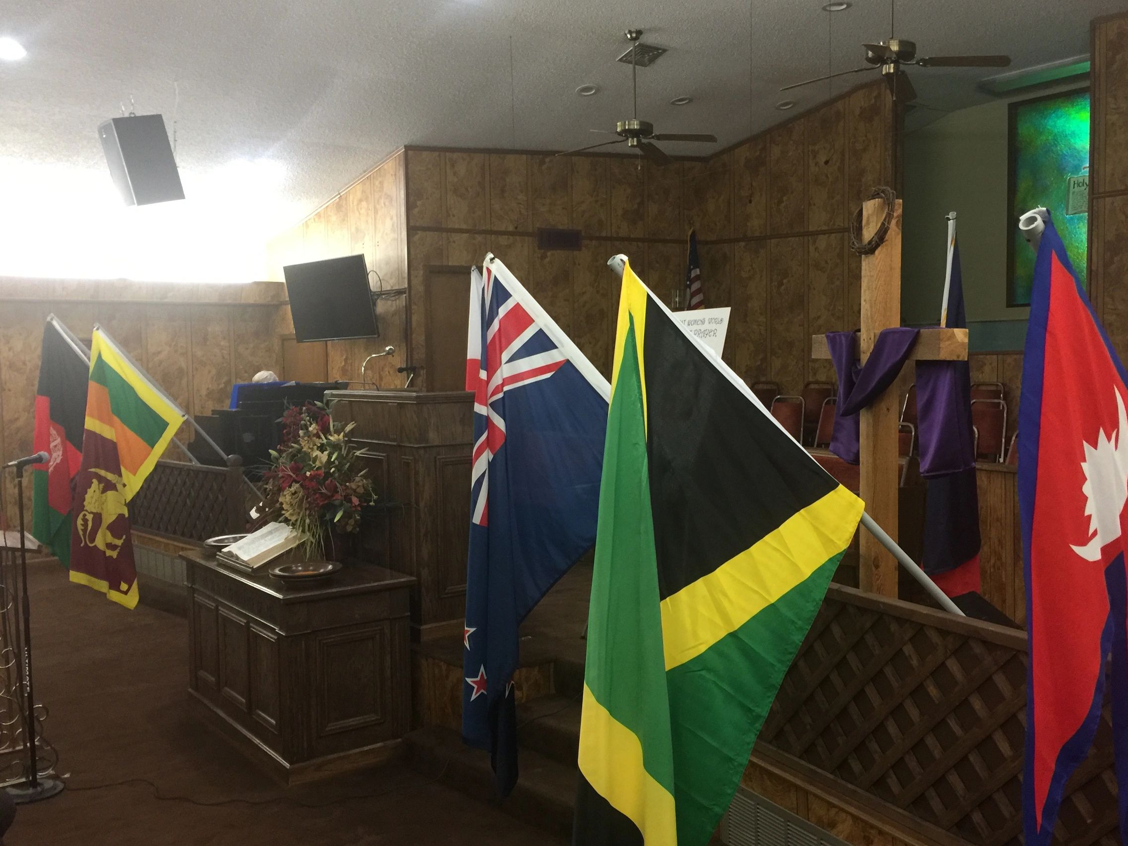 Flags displayed in a church with a wooden cross and pulpit.