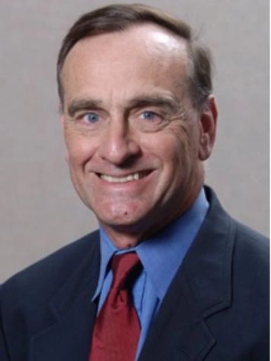 Smiling man in a suit and red tie against a plain background.