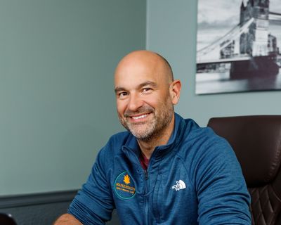 Smiling bald man in a blue jacket sitting indoors.