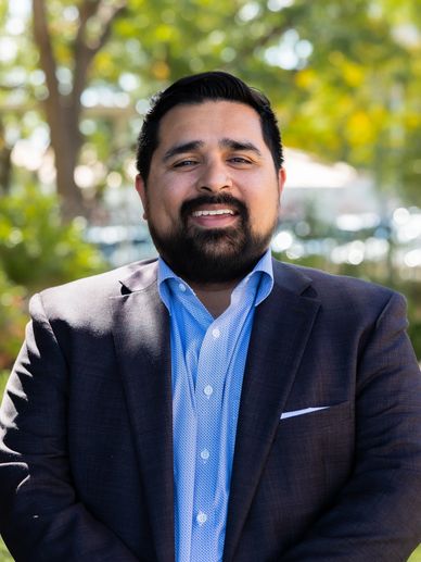 Smiling man in a suit jacket outdoors in daylight.