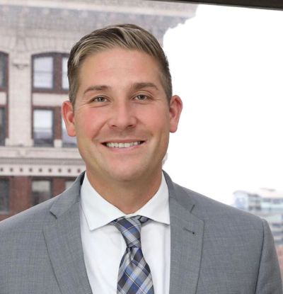 Professional man in a gray suit smiling in front of a cityscape.