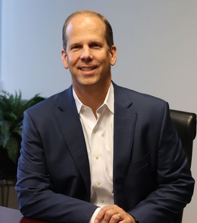A smiling man in a navy suit sitting at a desk.