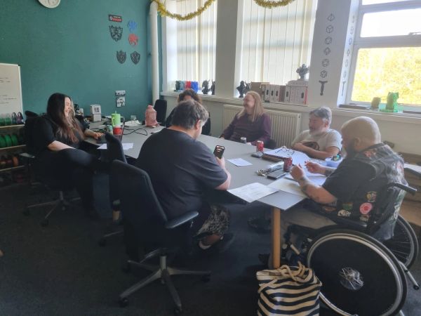 Five people engaged in a meeting around a table in a bright room.