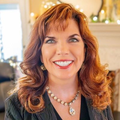 Smiling woman with red hair and jeweled necklace indoors.