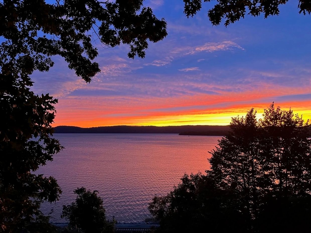 Sunset over a calm lake framed by trees.