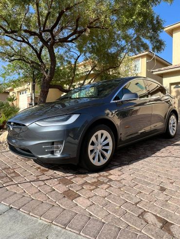 A sleek gray Tesla Model X parked on a cobblestone driveway.