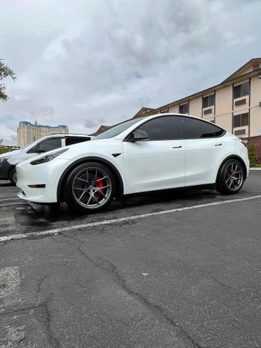 White Tesla Model Y with tinted windows and custom wheels parked outdoors.