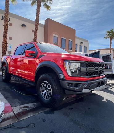 Red Ford pickup truck parked outside a building with palm trees.