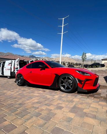 Sleek red sports car with black accents parked on a sunny driveway.