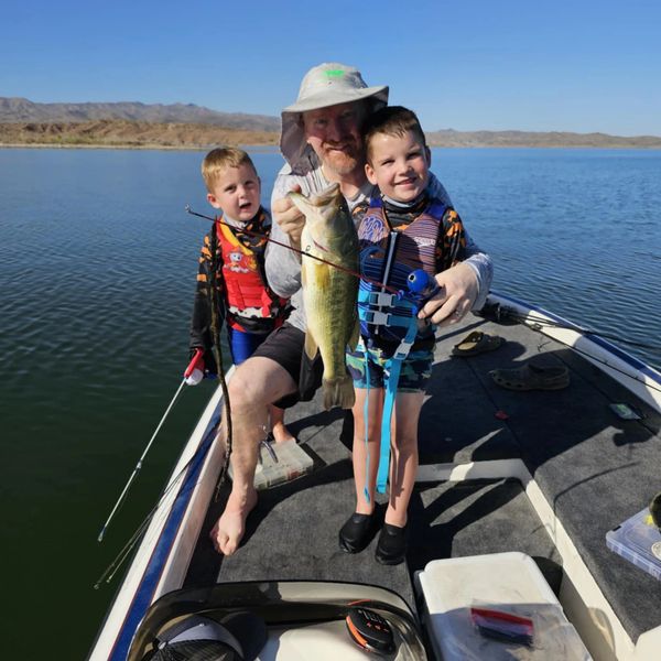A man and two boys on a boat proudly holding a large fish they caught.