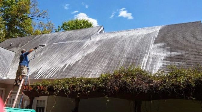Worker soft-washing a shingle roof.