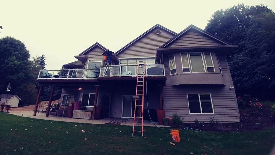 Worker on a ladder servicing the upper roofline of a two-story house.