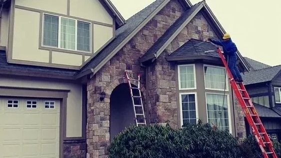 Worker on a ladder servicing the roofline of a two-story house.