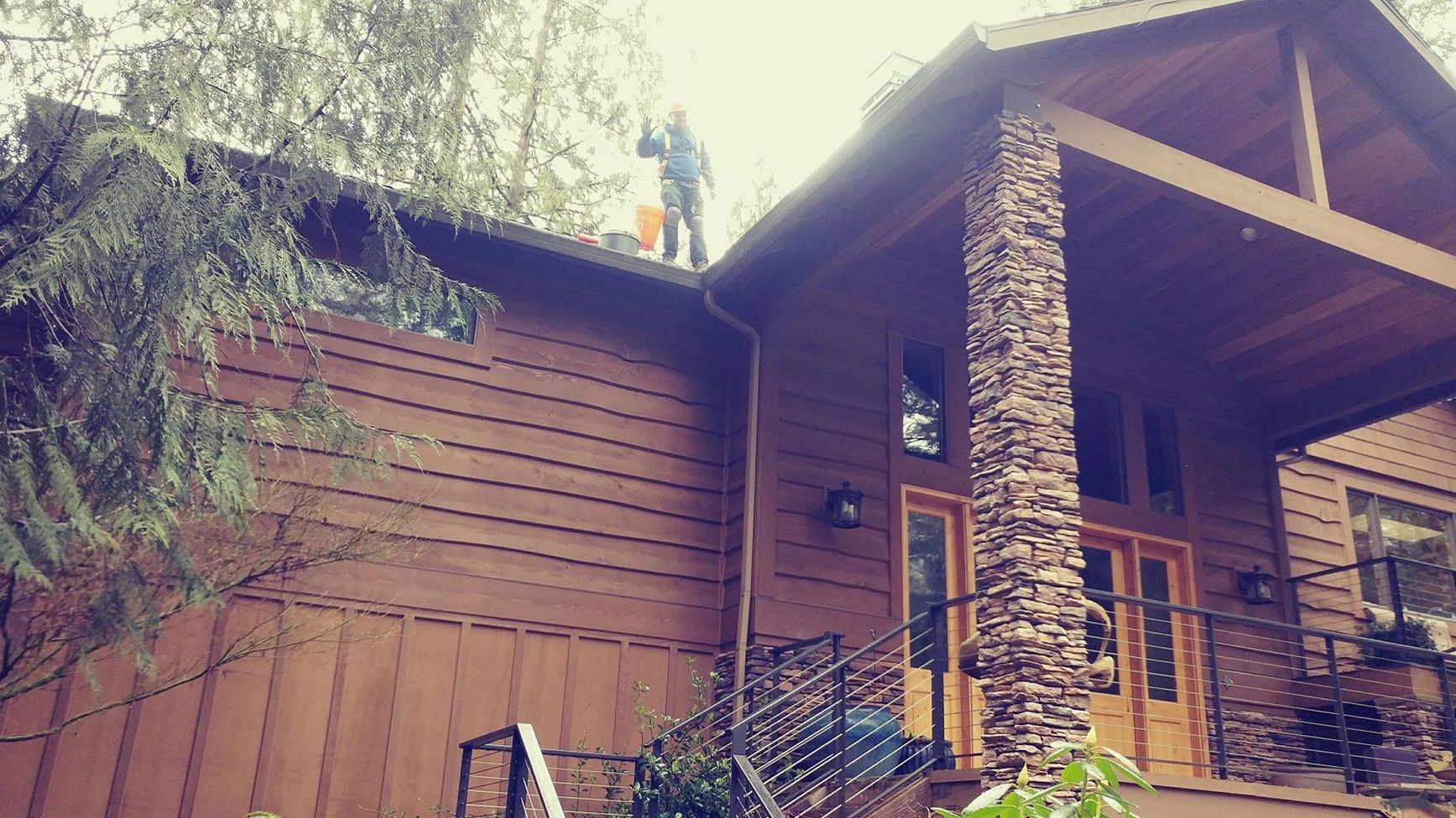 Worker standing near the gutter on the roof of a large house.