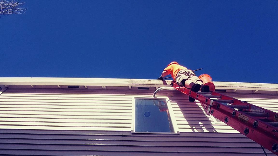 Worker on an extension ladder cleaning a second-story gutter.