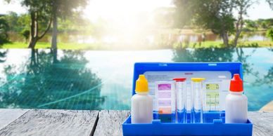 Pool water testing kit on wooden deck near a sunny pool.