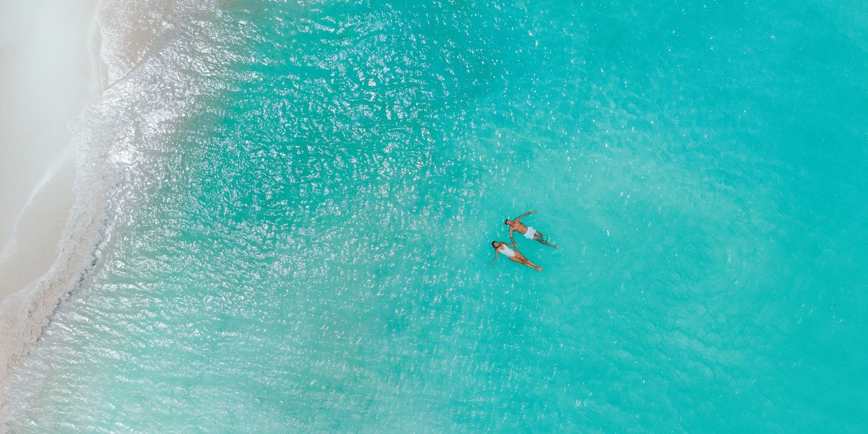 A couple floating peacefully in clear turquoise ocean water near the white sands of Eagle Beach, Aruba.