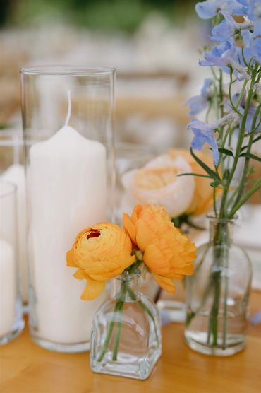 Orange ranuculus and blue delphinium designed in bud vases.