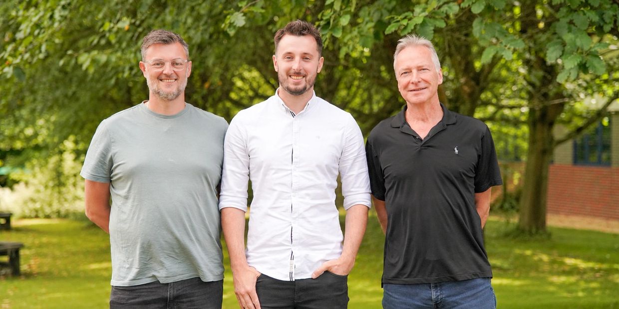 Three men standing outdoors with smiles.