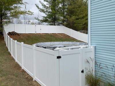 White vinyl fencing installed on a sloped backyard. The fence also has a gate with black hardware.