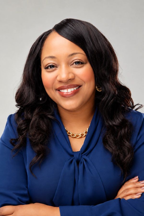 Smiling woman in blue blouse with gold jewelry.