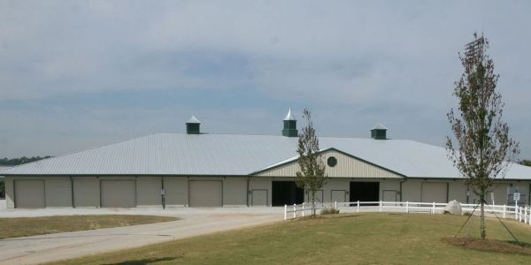Large barn with multiple garage doors and white fencing.