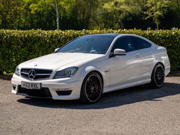 White Mercedes-Benz coupe parked on a paved surface with greenery in the background.